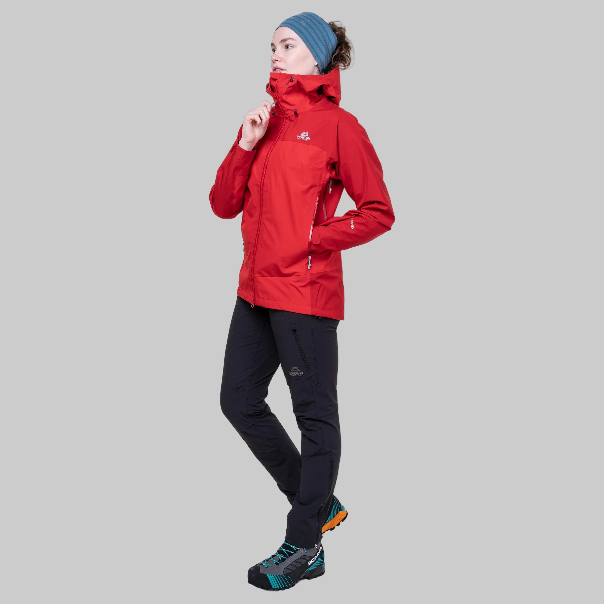 Model wearing a red waterproof jacket with Mountain Equipment badge and black pants on a white background