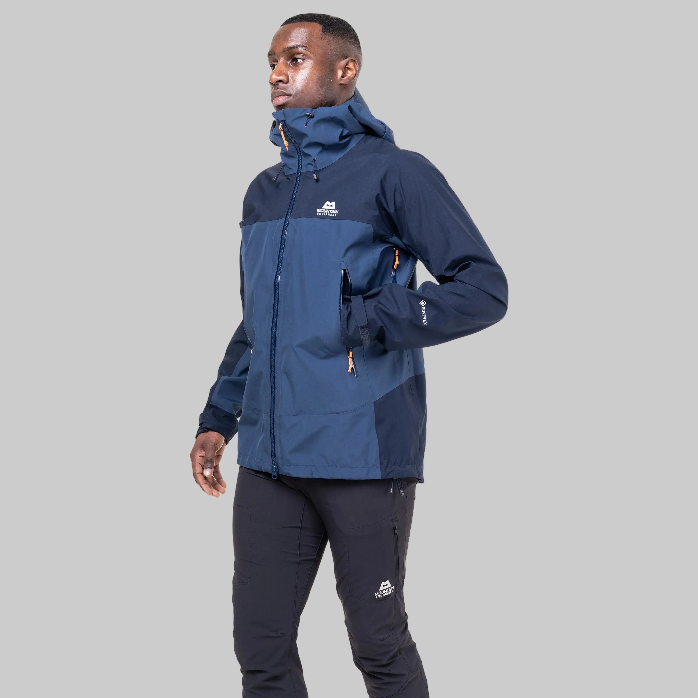 A man wearing a navy blue and slate blue technical outdoor jacket with matching dark pants, shown from the waist up against a plain white background.