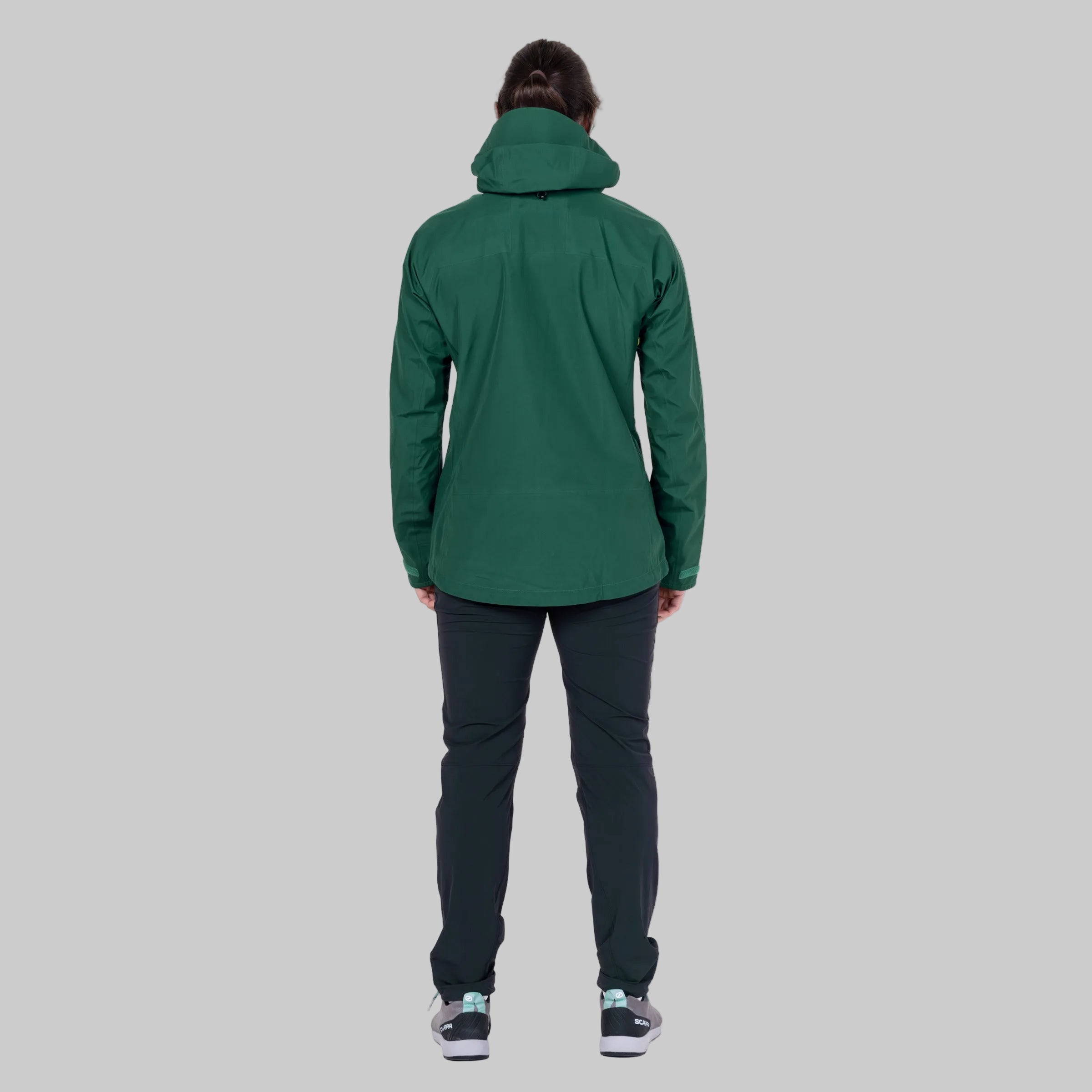 A person shown from the back wearing a dark green hooded jacket, dark pants, and sneakers against a plain white background.