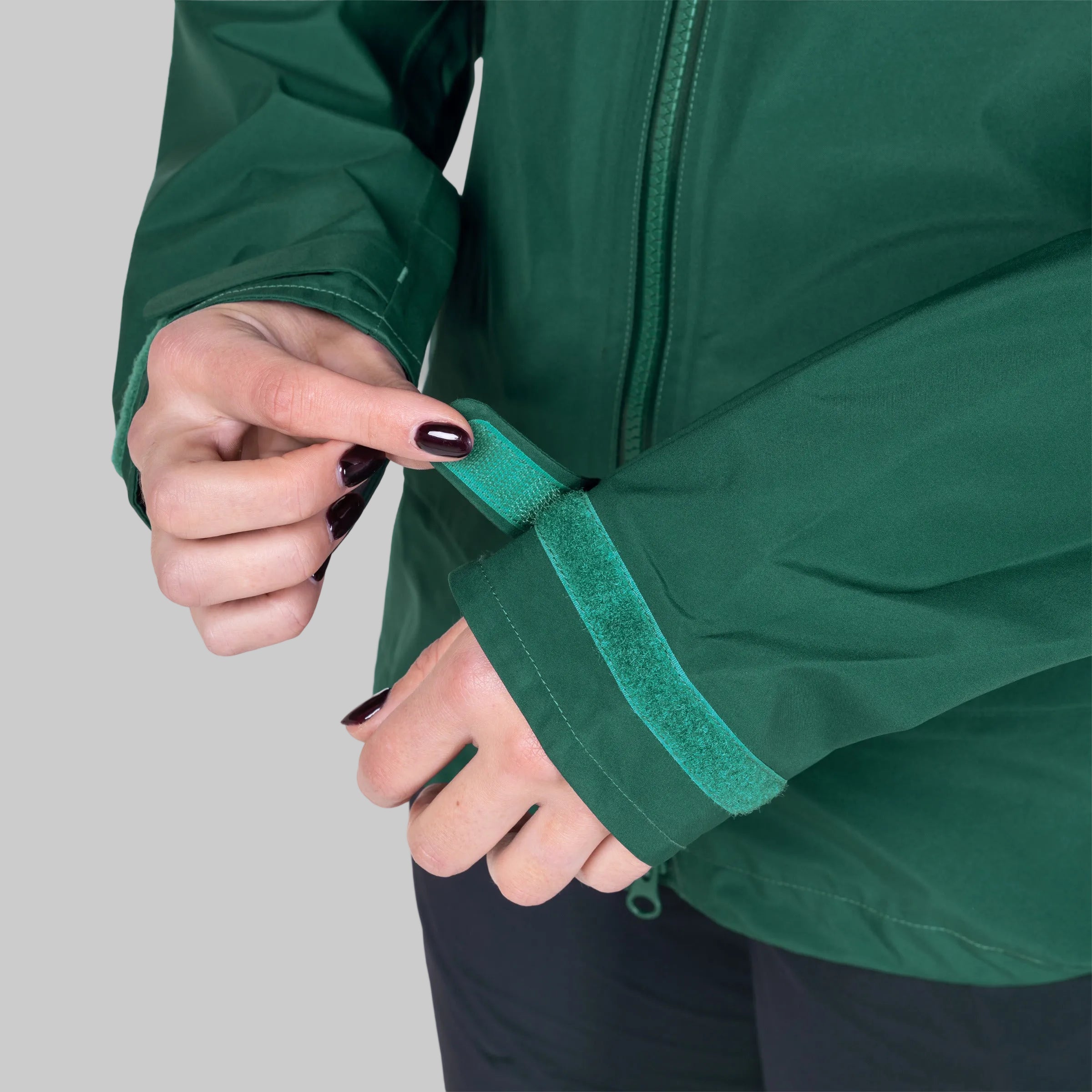 Close-up of a person wearing a dark green waterproof jacket, demonstrating the adjustable hook-and-loop wrist strap on the cuff.