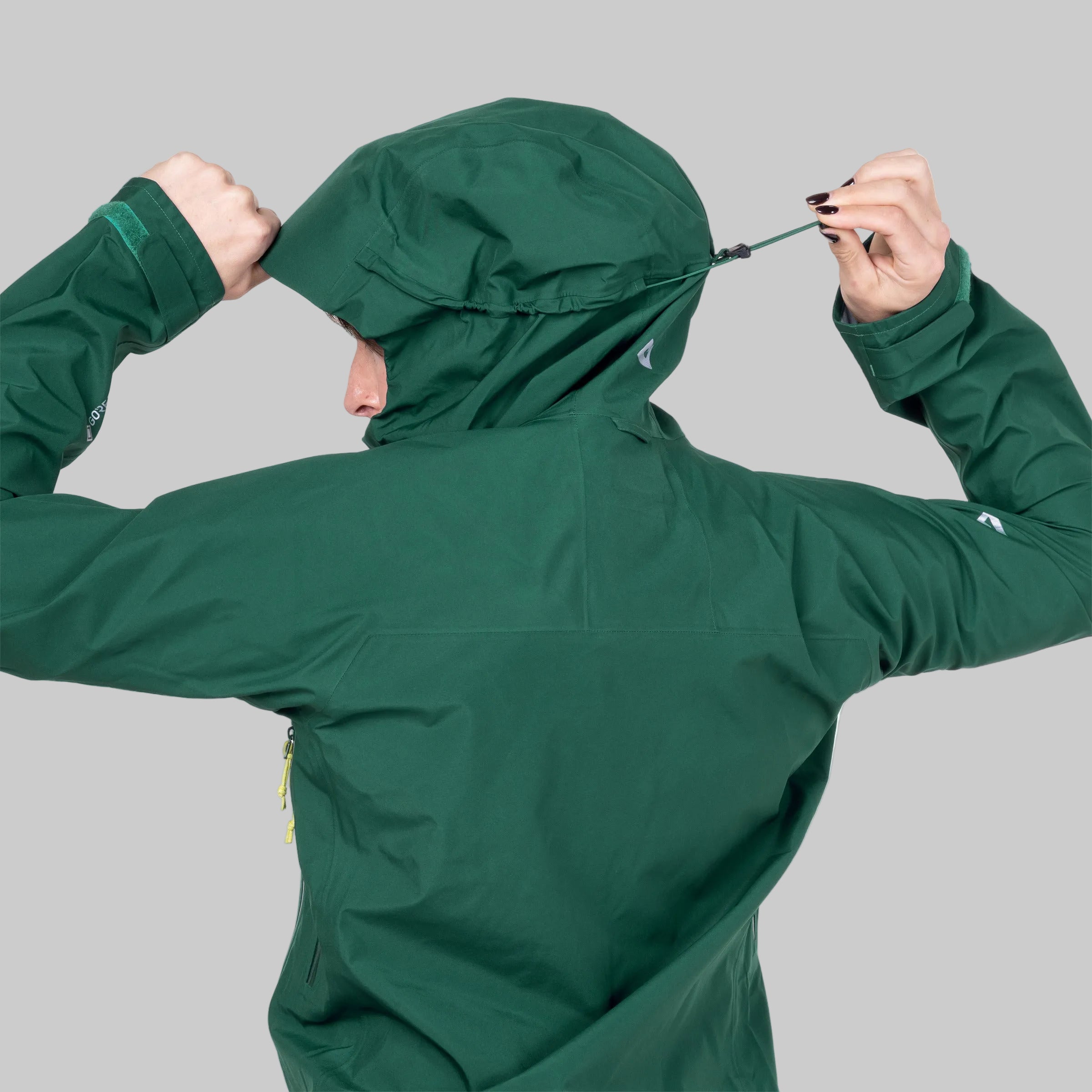 Person wearing a green jacket with a hood, adjusting it on a white background