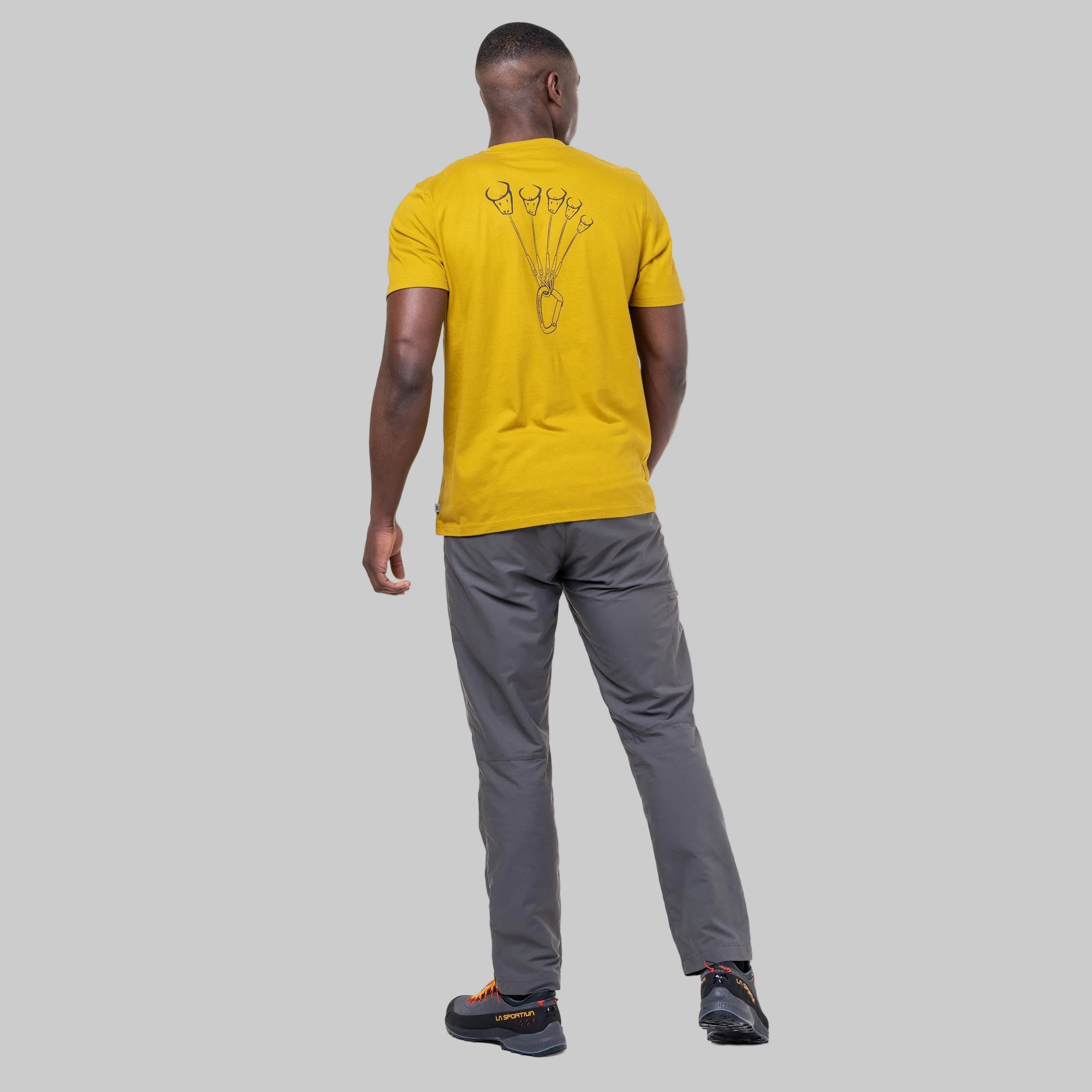 A man viewed from behind wearing a bright yellow t-shirt with a black graphic on the back, gray pants, and black sneakers, set against a plain white background.