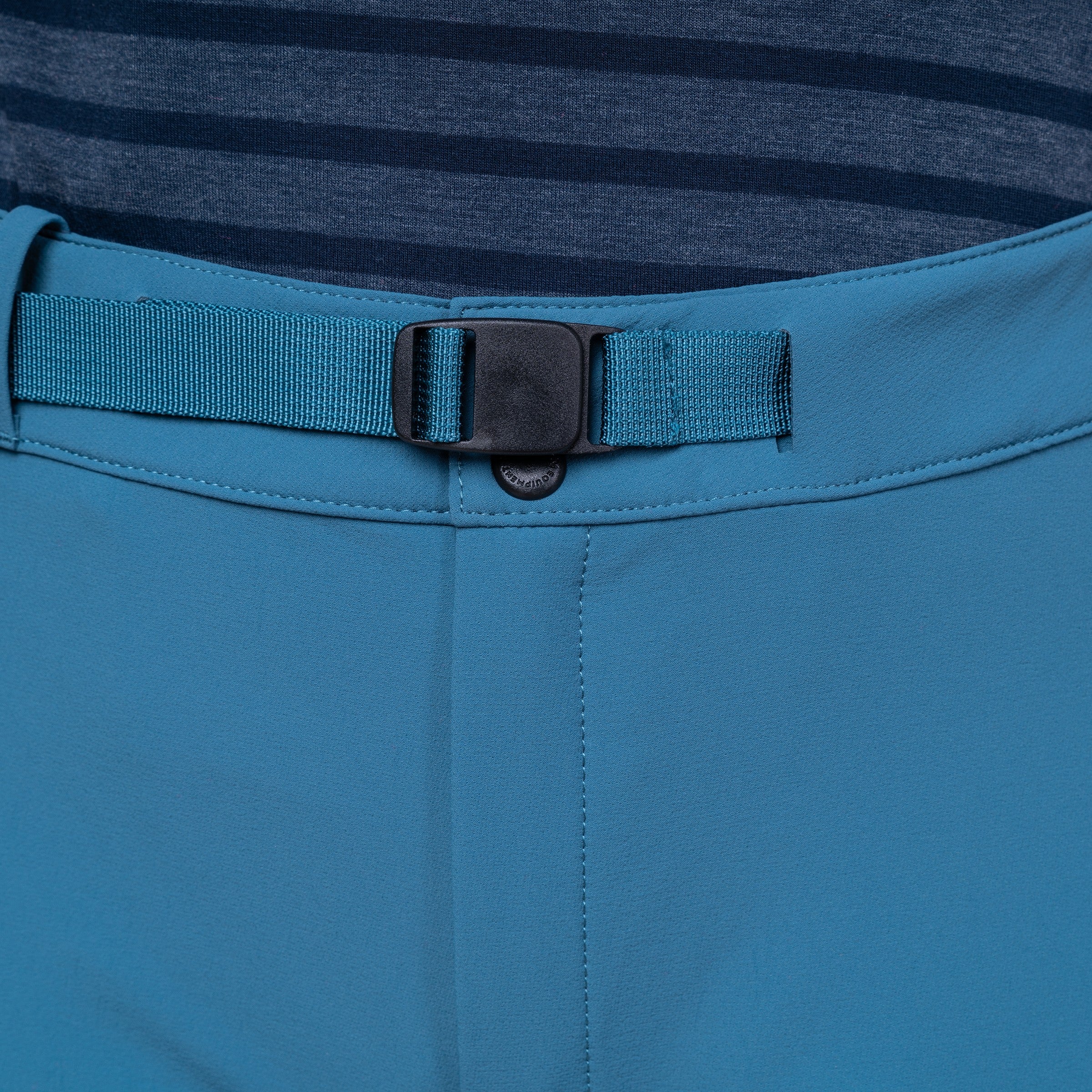 Close-up of a pair of blue outdoor pants showing the waistband with a matching blue webbing belt and black plastic buckle, worn over a dark blue striped shirt.