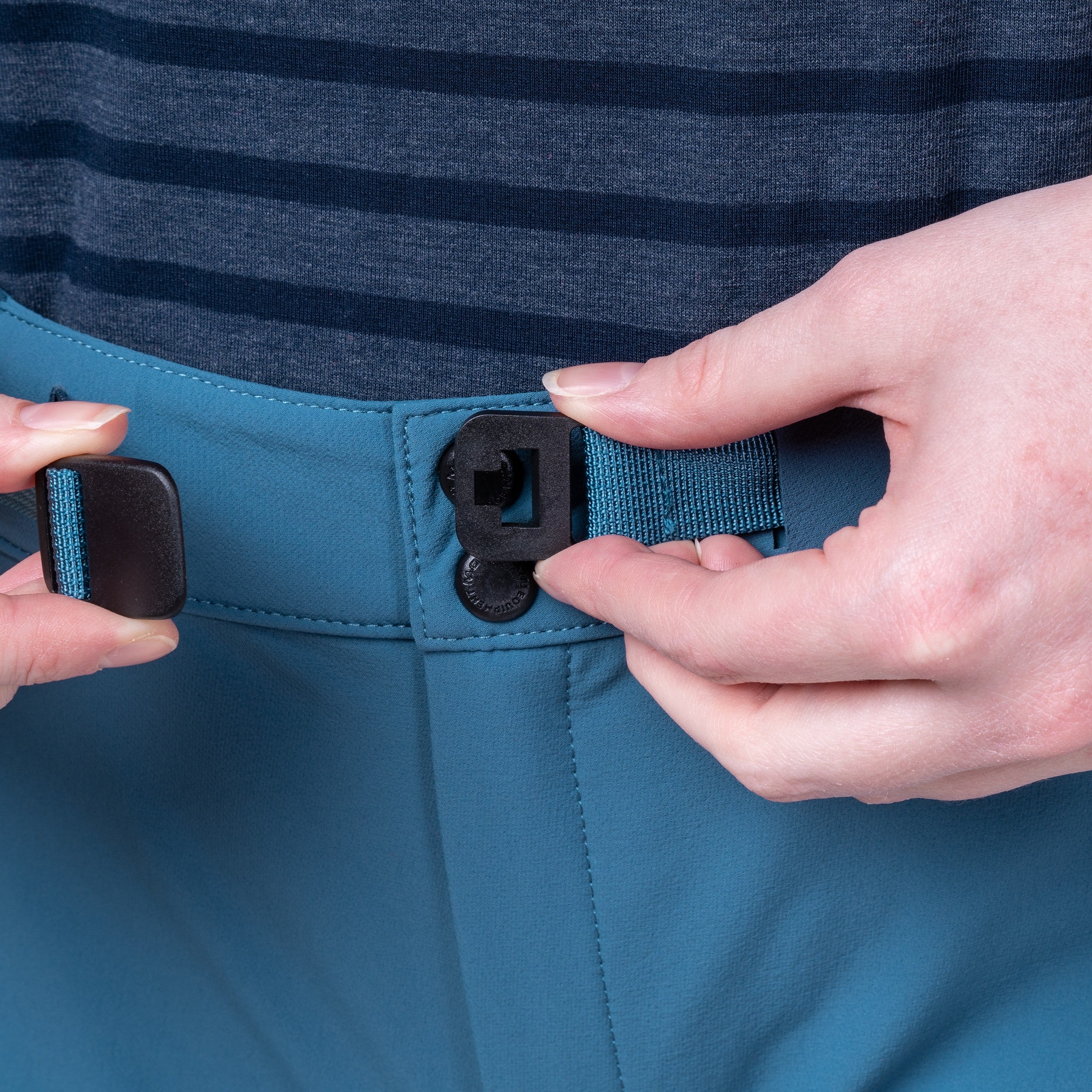 Close-up of a person fastening a teal waist belt with black plastic buckles over blue-gray striped trousers.