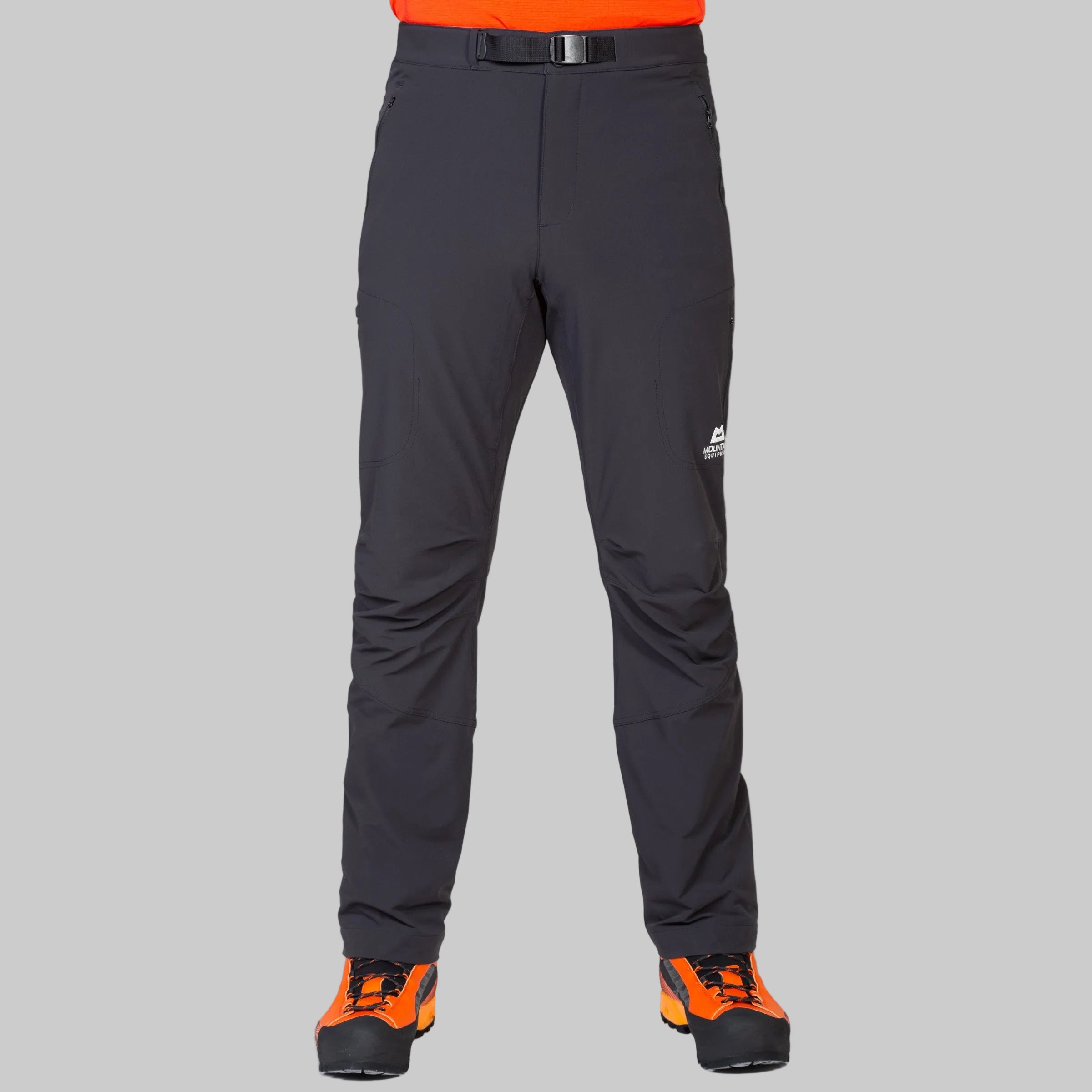 Black technical pants with a black belt and orange and black hiking boots, shown on a model from the waist down against a light gray background.