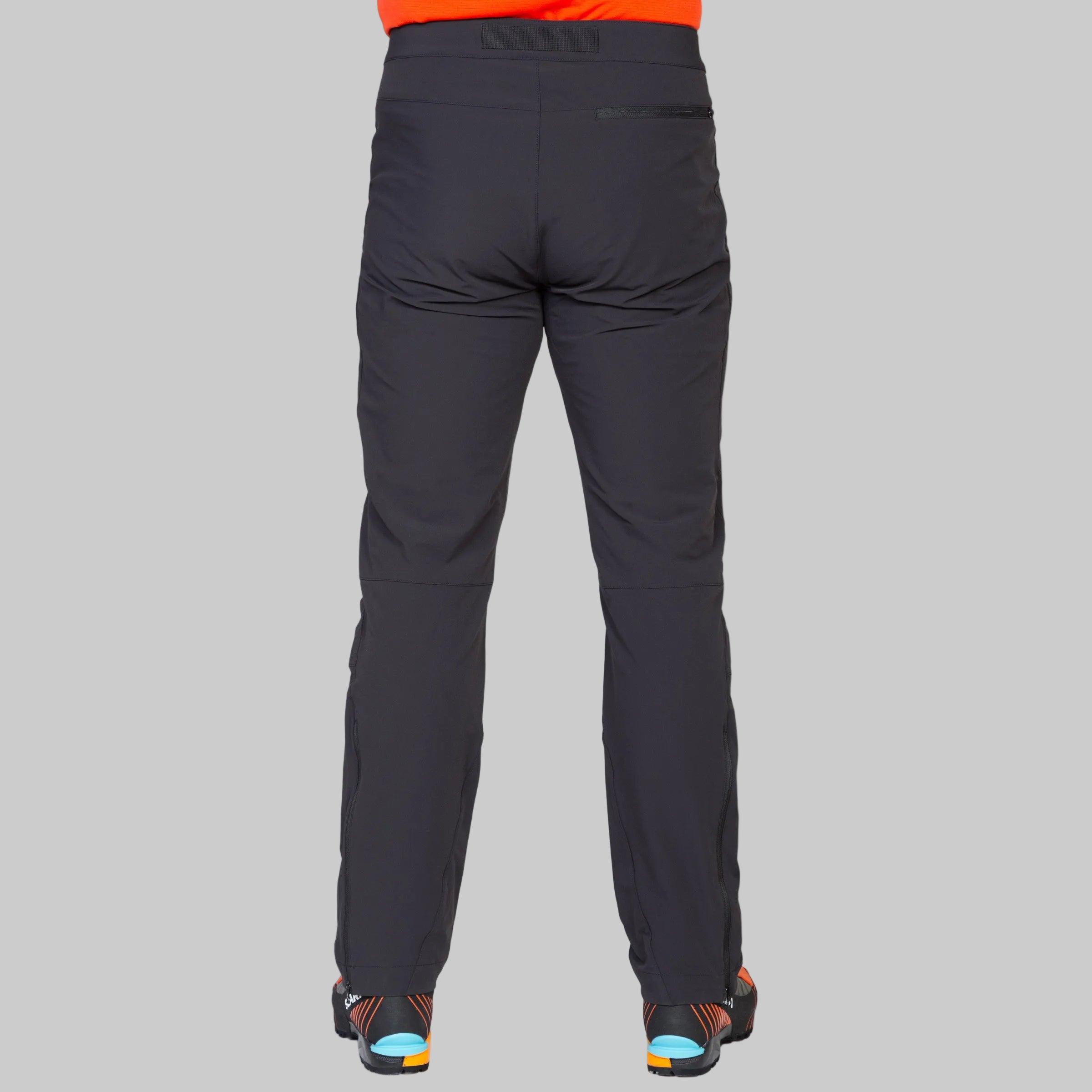 Rear view of a person wearing dark charcoal gray technical pants, shown against a light gray studio background.