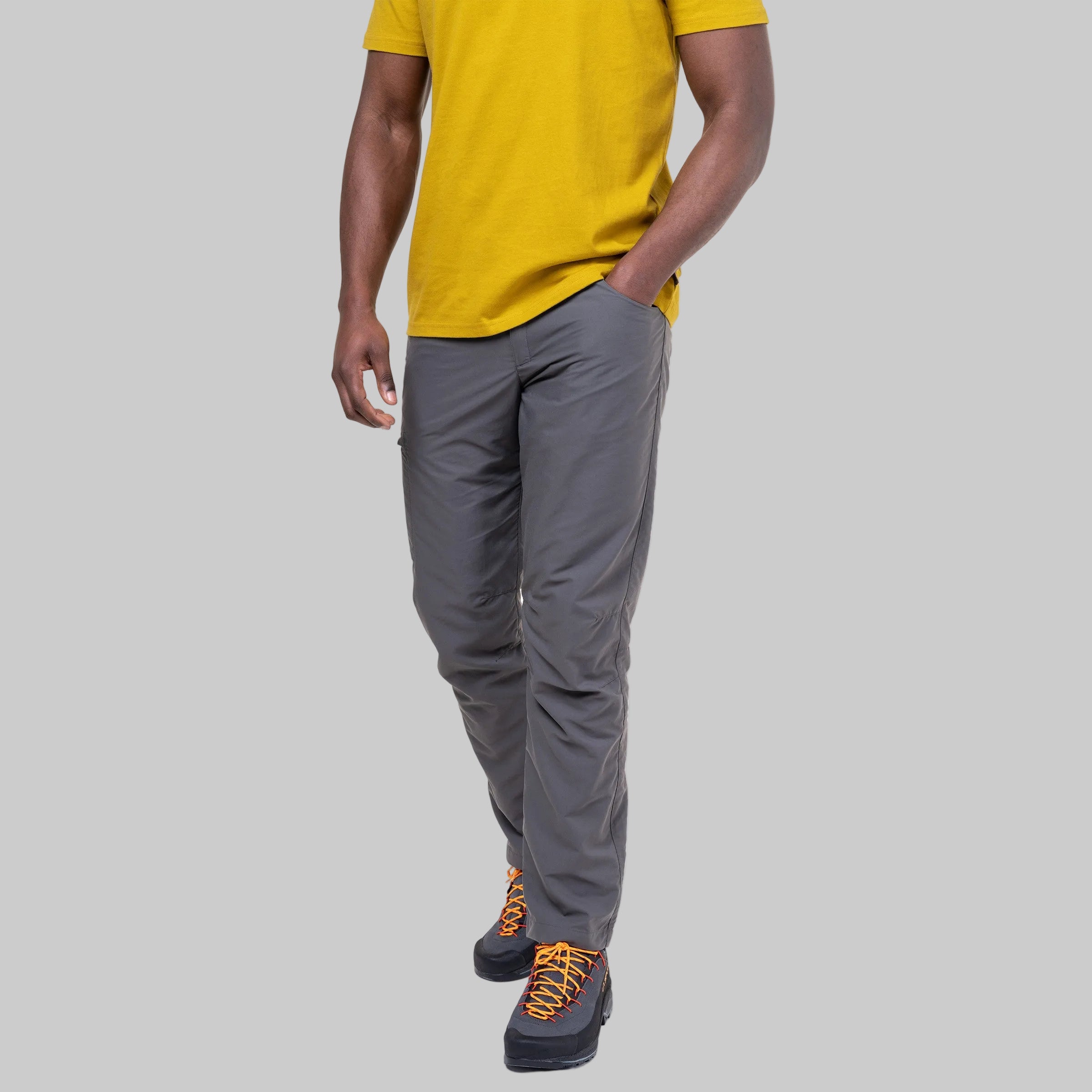 A person wearing gray slim-fit pants, a yellow t-shirt, and hiking shoes, shown from the waist down against a plain white background.