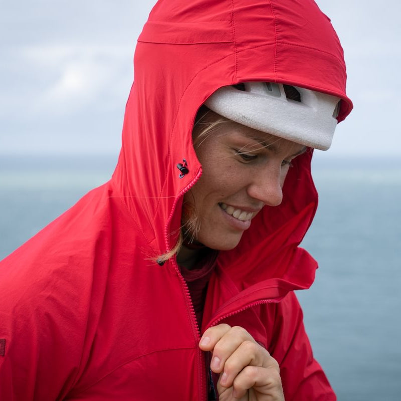 Person wearing a red raincoat with a hood, standing against a blurred natural background.